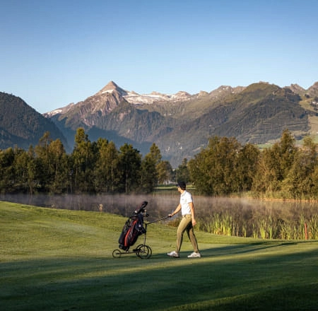 Golfspieler zieht Golfbag mit Berglandschaft im Hintergrund.