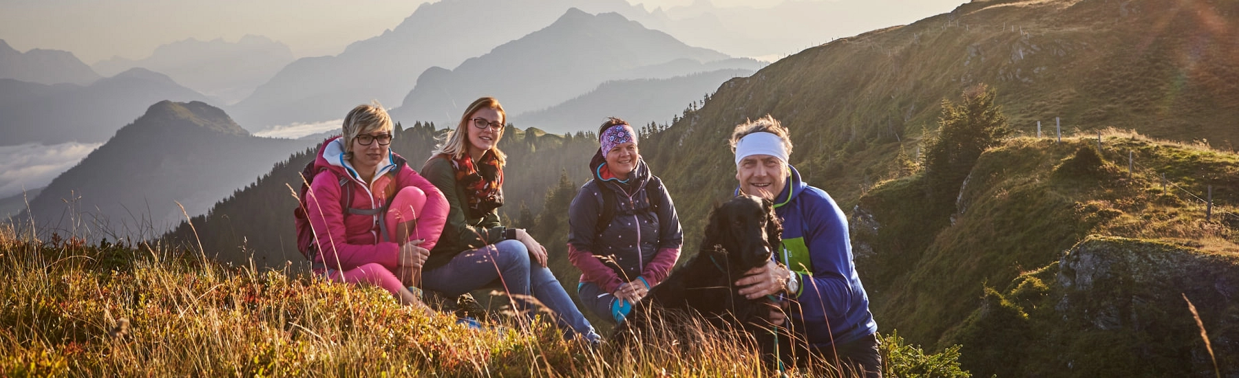 Vier Wanderer sitzen im Gras mit Bergen im Hintergrund